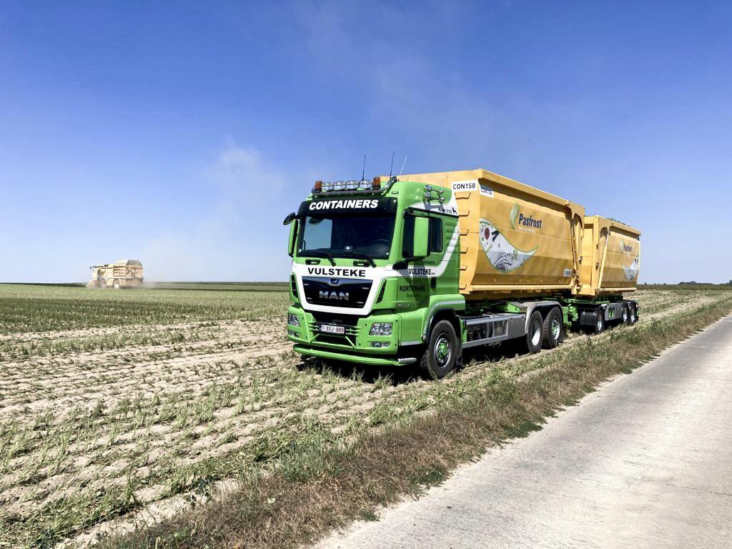 Vulsteke chauffeur CE die met een vrachtwagen met afzetcontainer rijdt op een veld